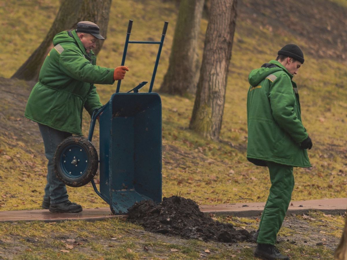 Twee hoveniers van Groene Tuinen rijden met een kruiwagen door een park
